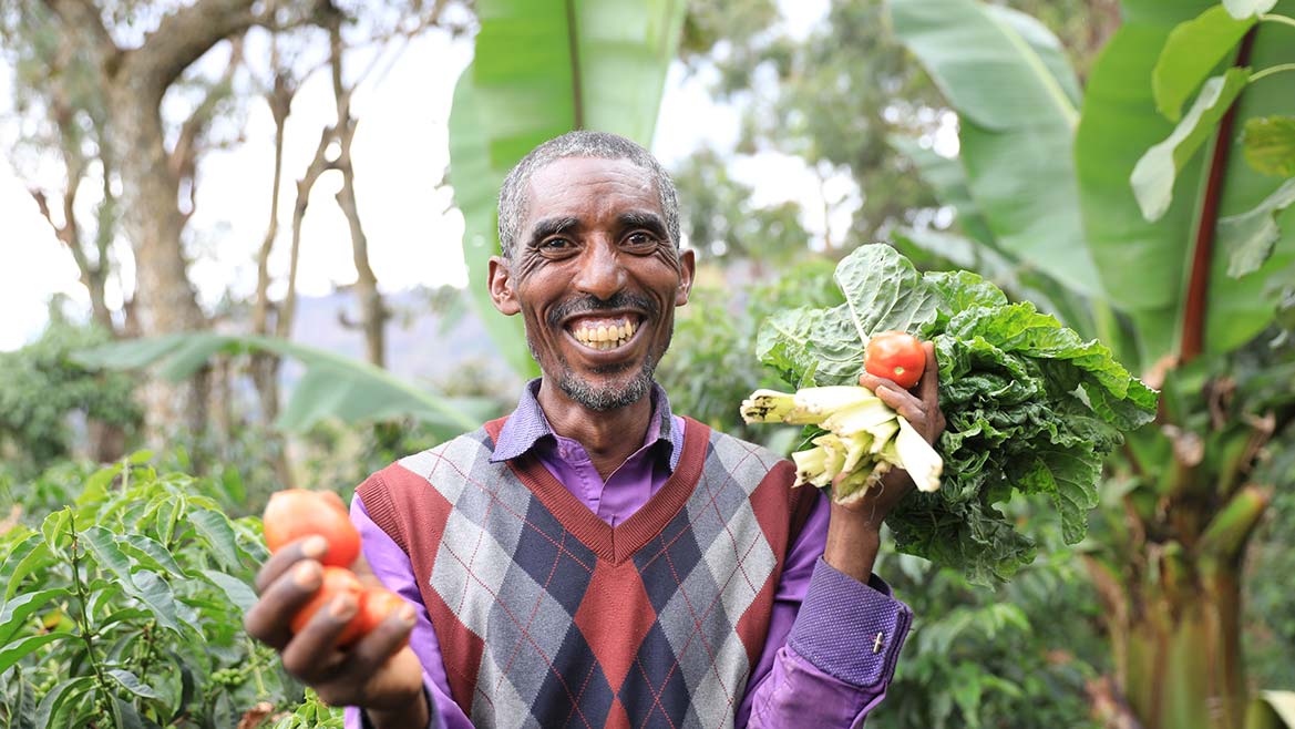 Mann in Äthiopien grinst und hält Obst und Gemüse in den Händen