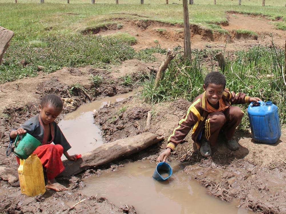 Zwei Kinder schöpfen Wasser aus einer Wasserstelle.