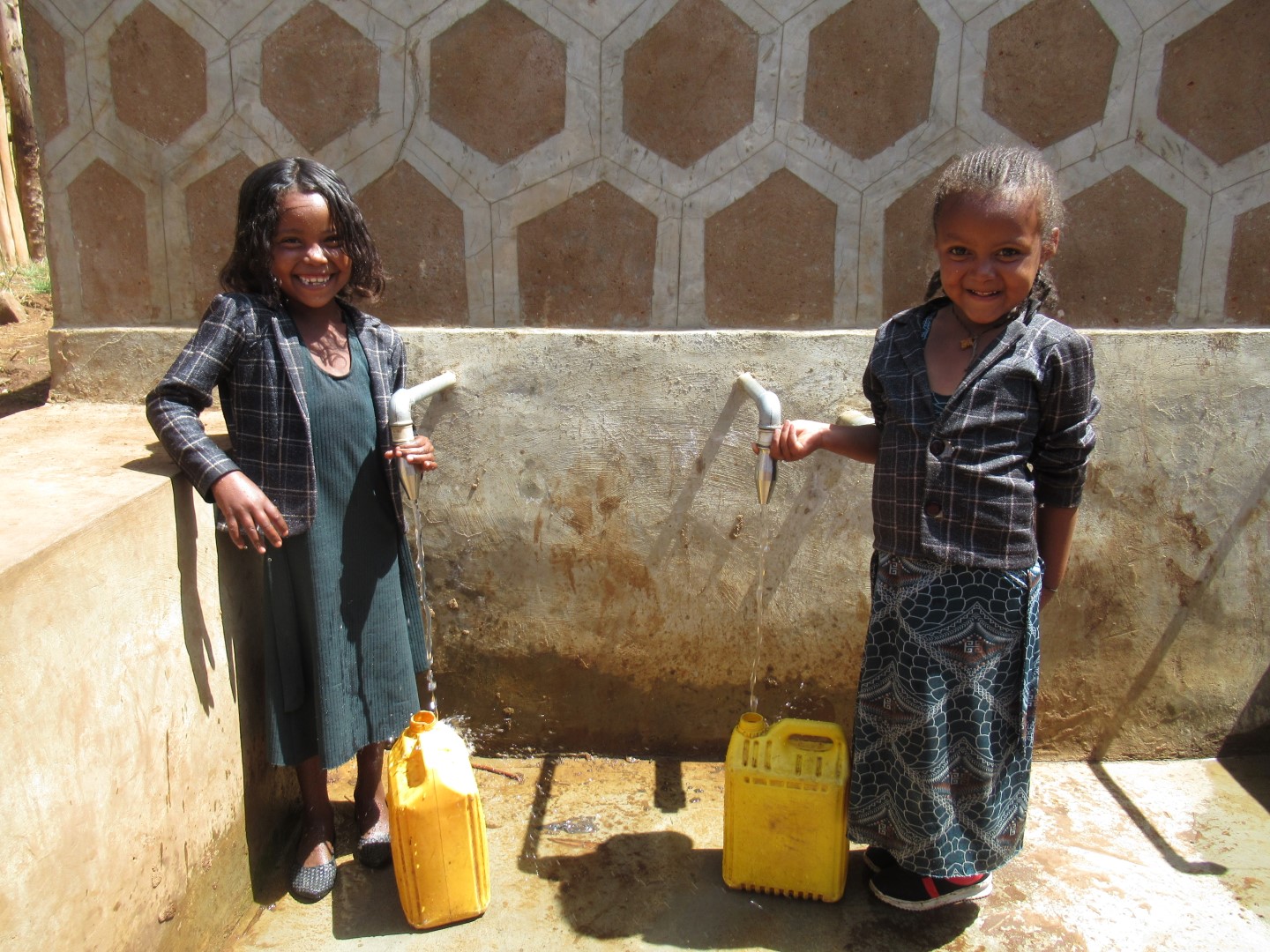 Mädchen mit einem gelben Kanister füllt Wasser aus einem Brunnen ab