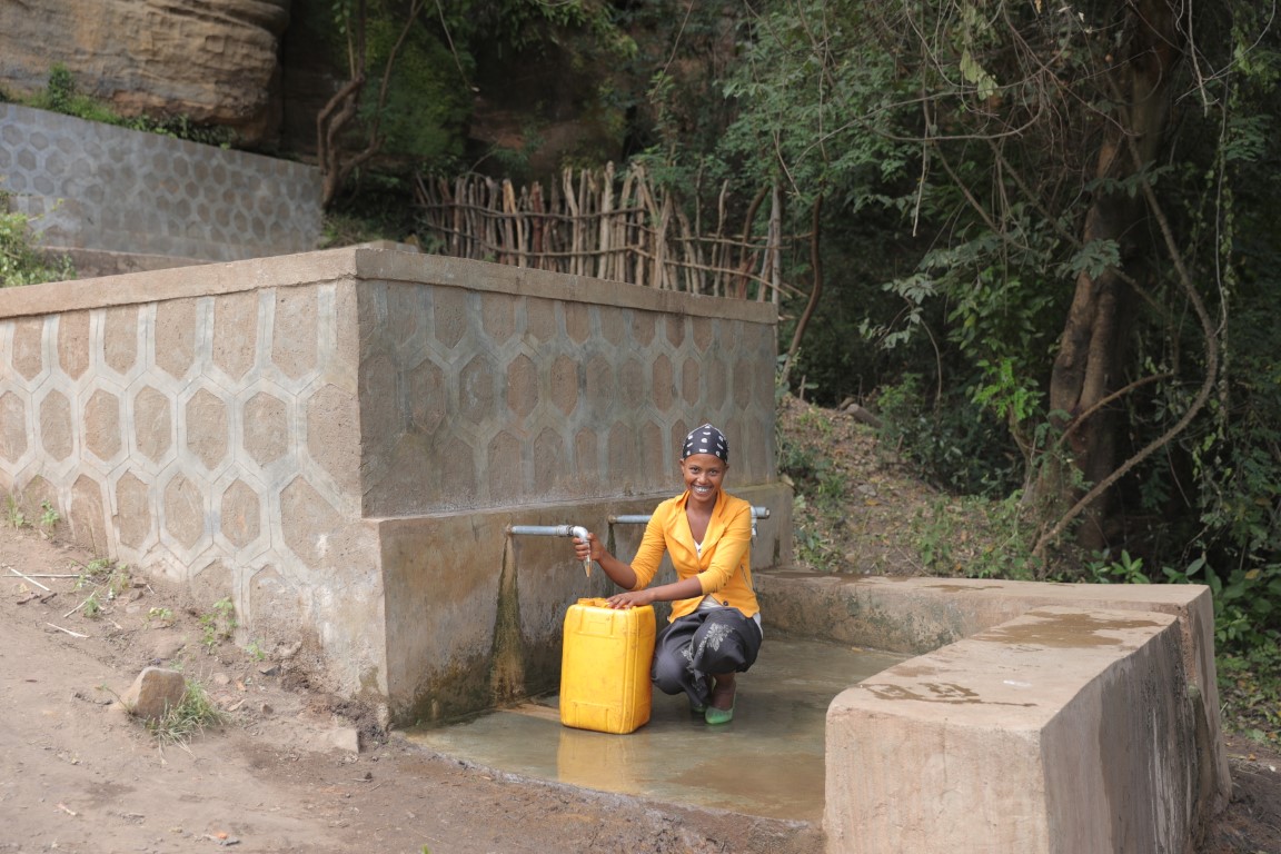 Frau mit gelben Kanister füllt Wasser für Menschen für Menschen ab