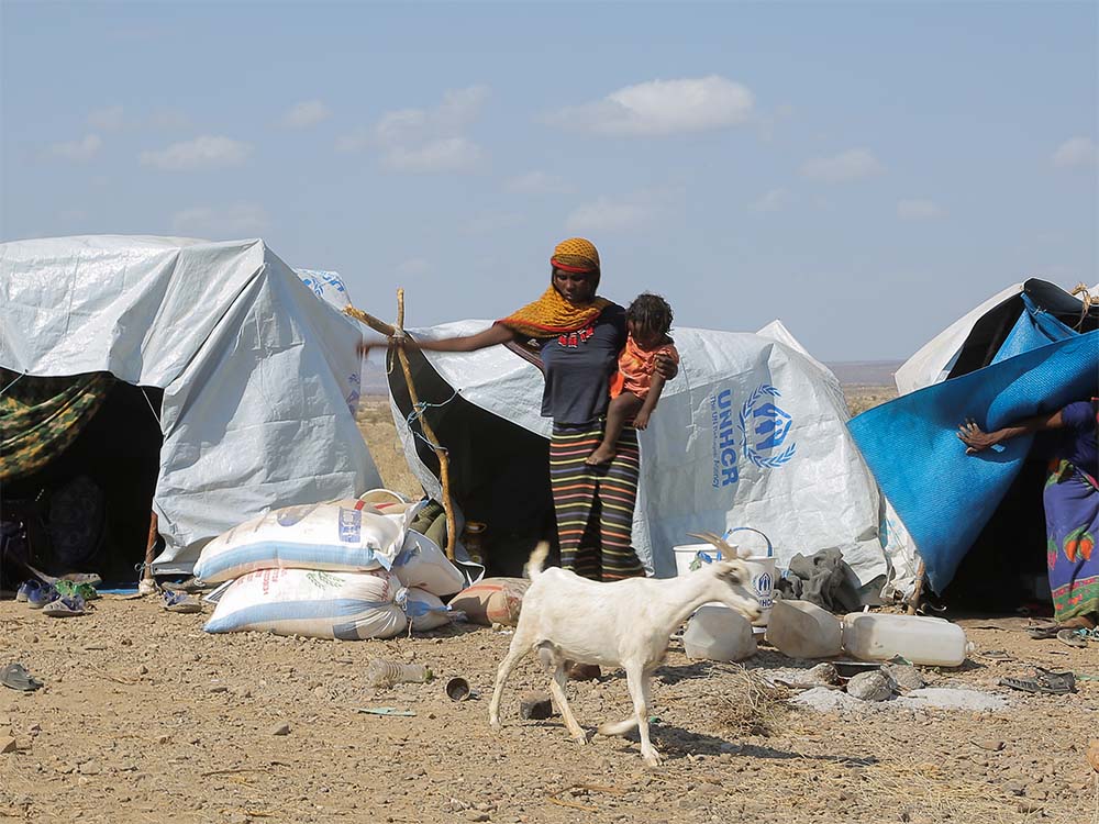 Eine Frau in Äthiopien steht in einem provisorischen Zeltlager mit ihrem Kind und einer Ziege