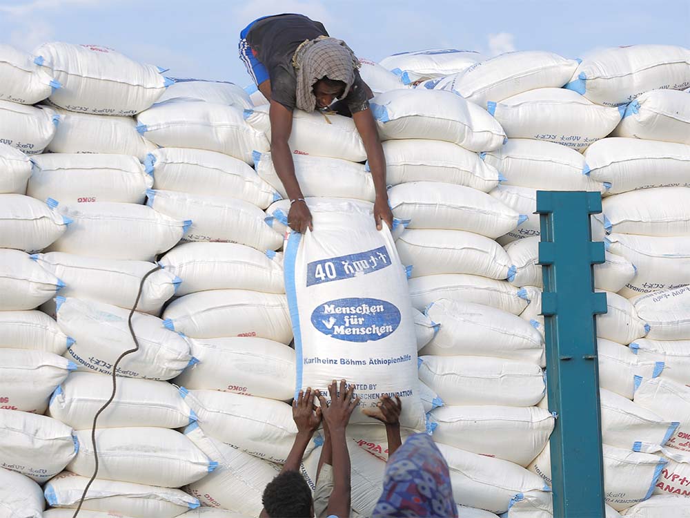Ein Mann in Äthiopien reicht einen Sack mit Nothilfe Gütern von einem Stapel