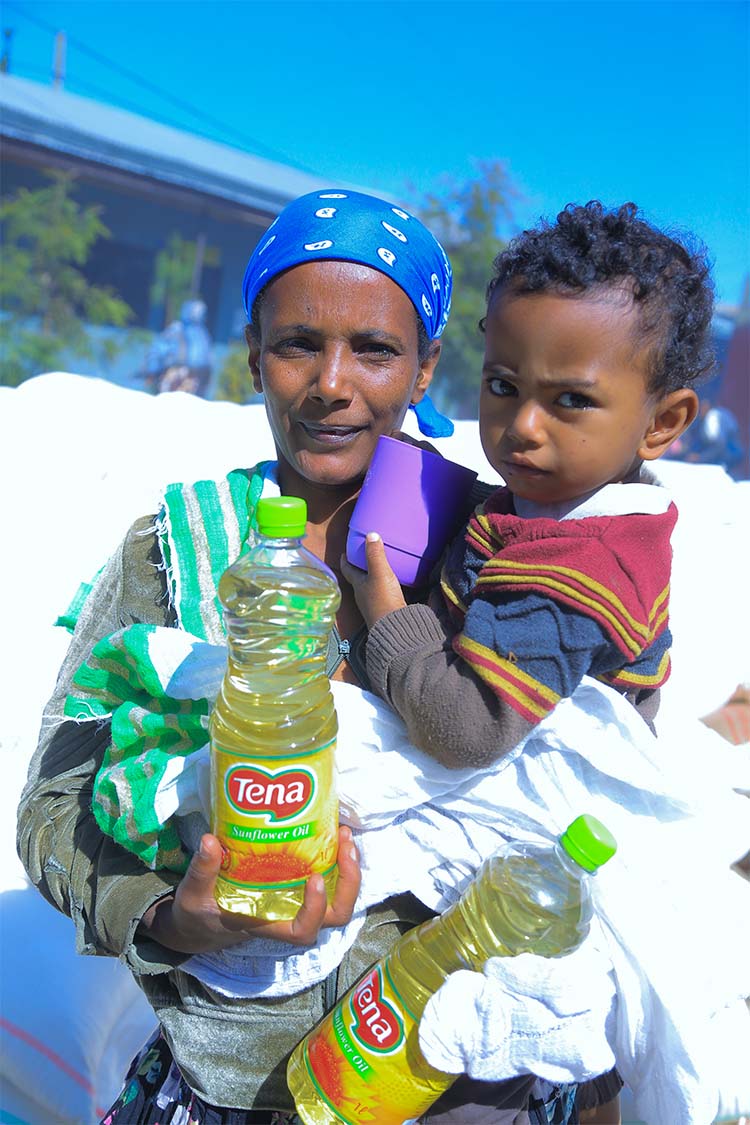 Eine Frau in Äthiopien steht mit ihrem Kind im Arm und hält zwei Falschen Öl als Nothilfe