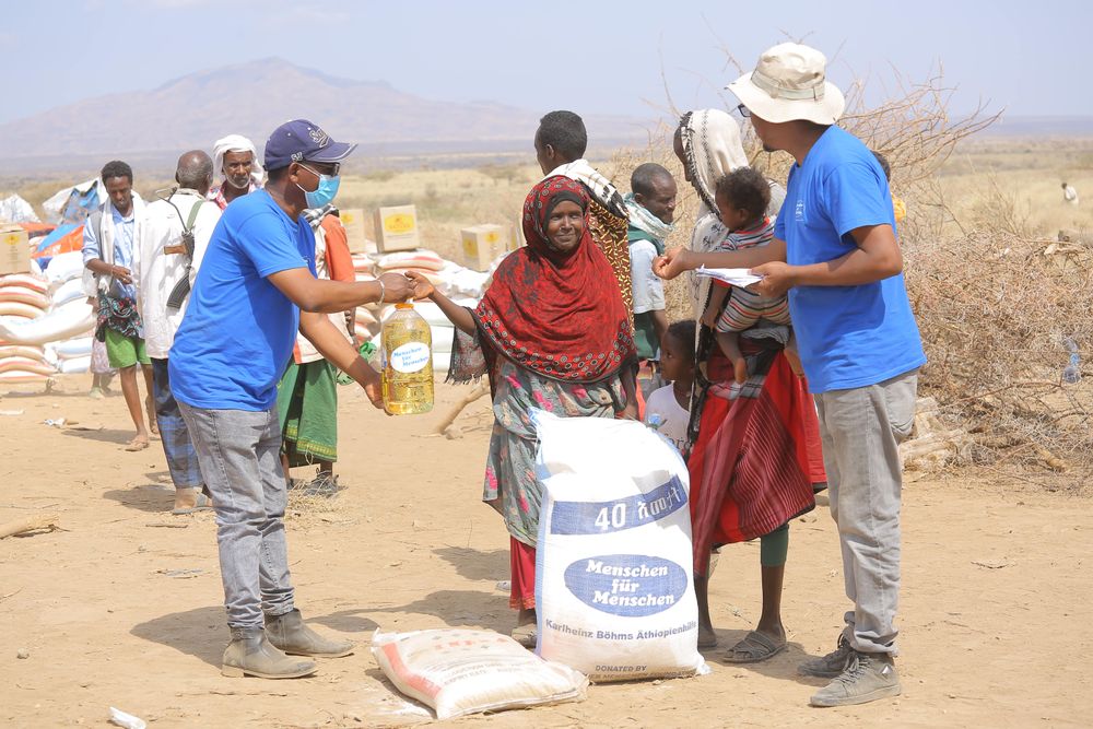 Eine Frau in einem äthiopischen Flüchtlingslager erhält einen Sack Getreide von Helfern in blauen T-Shirts