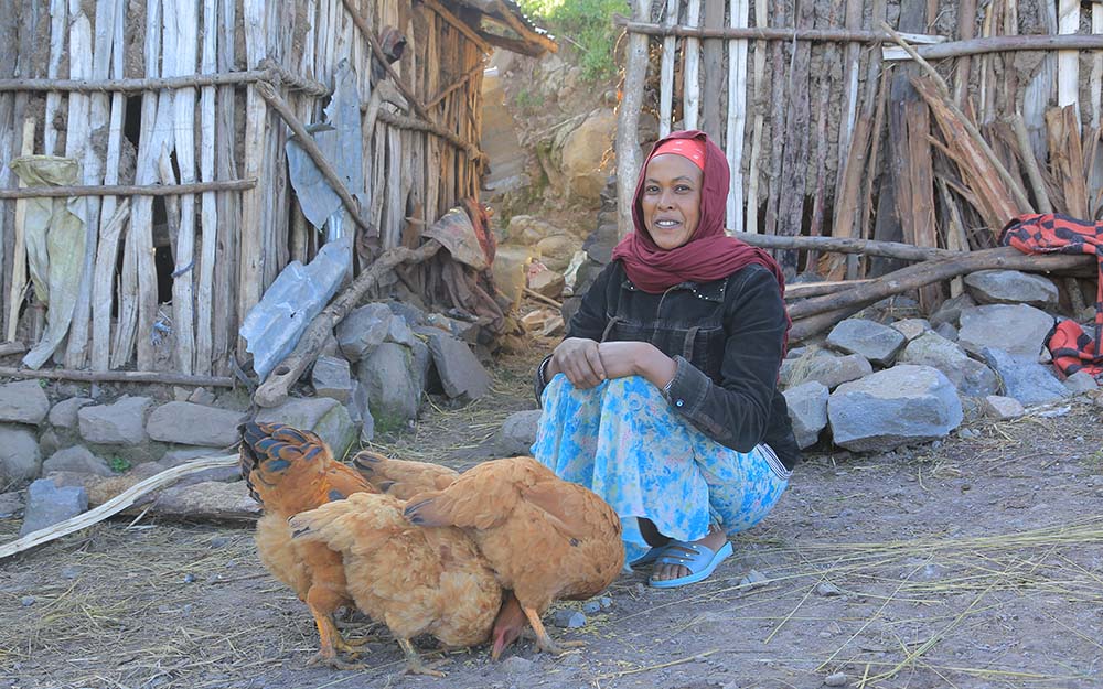 Frau mit drei Hühnern vor ihrer Hütte in Äthiopien
