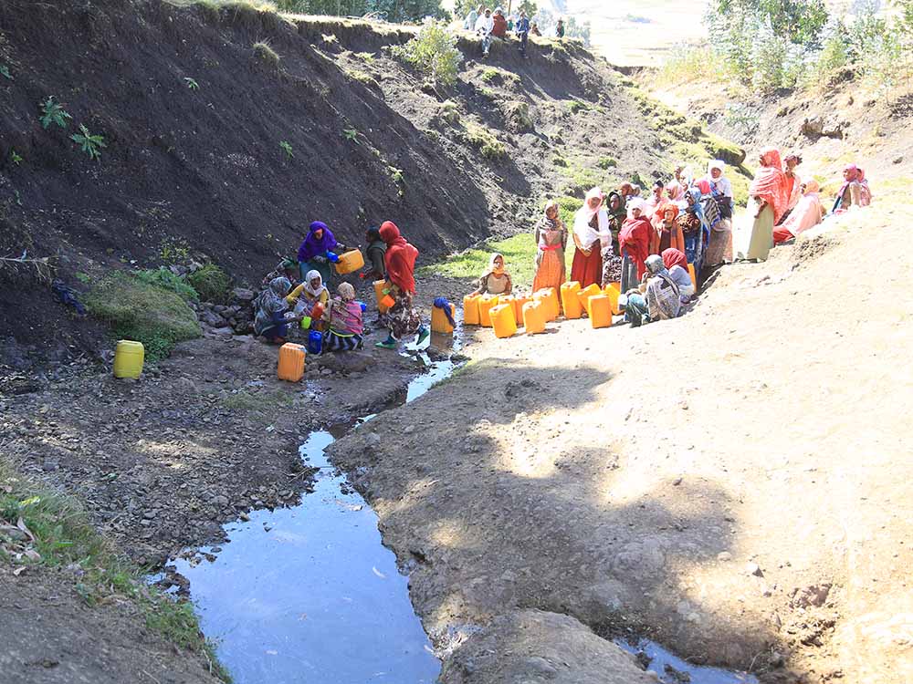 Frauen in Äthiopien schöpfen Wasser aus einem Rinnsal in gelbe Wasserkanister.