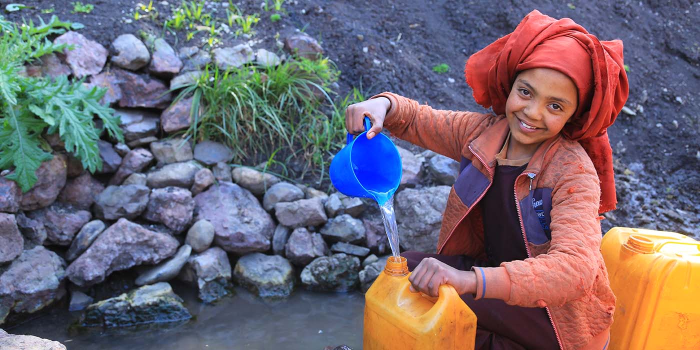 Äthiopisches Mädchen schöpft Wasser aus einem Rinnsal in einen gelben Wasserkanister.