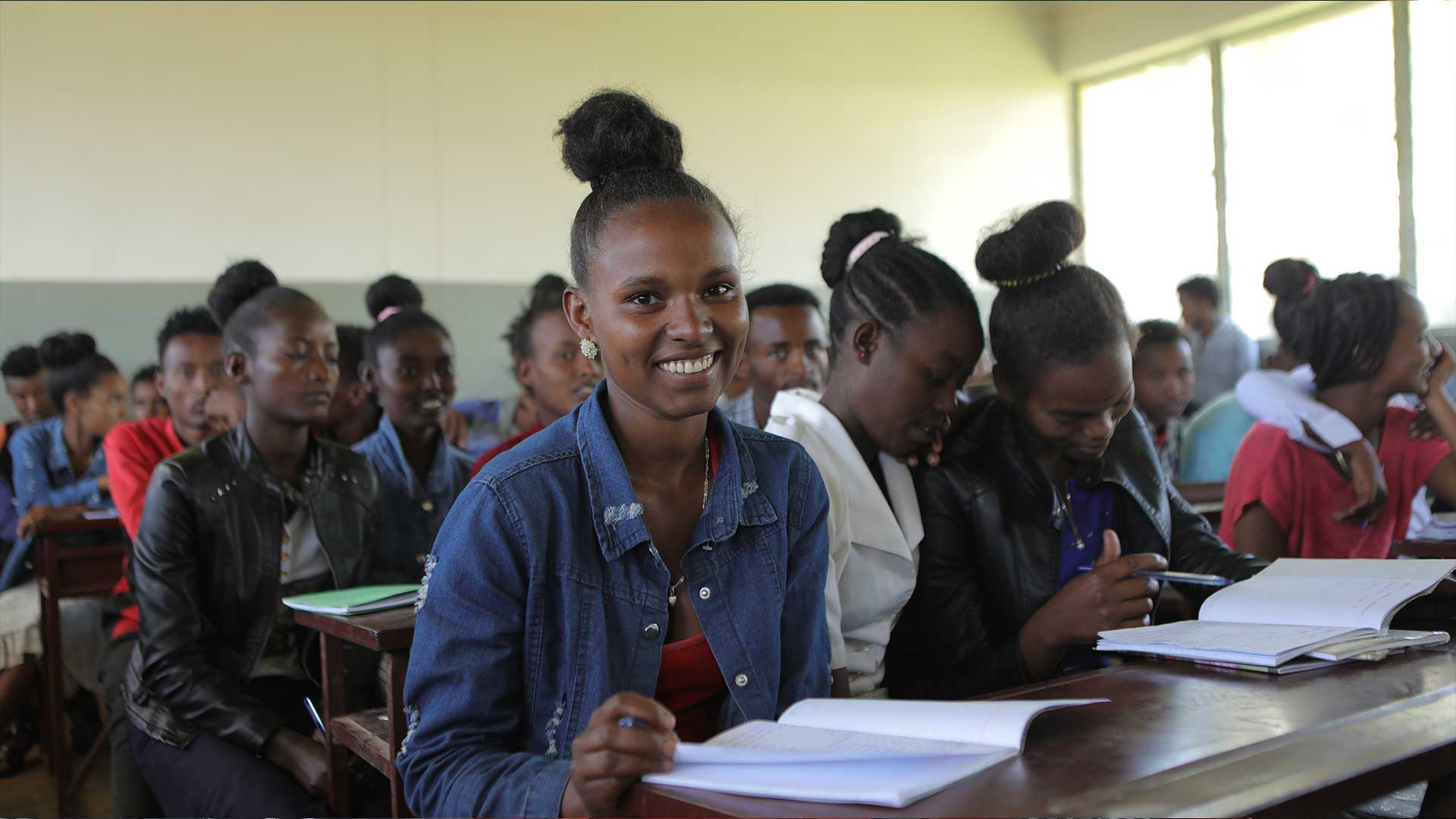 Tigist, eine äthiopische Schülerin sitzt an einer Schulbank und lächelt in die Kamera