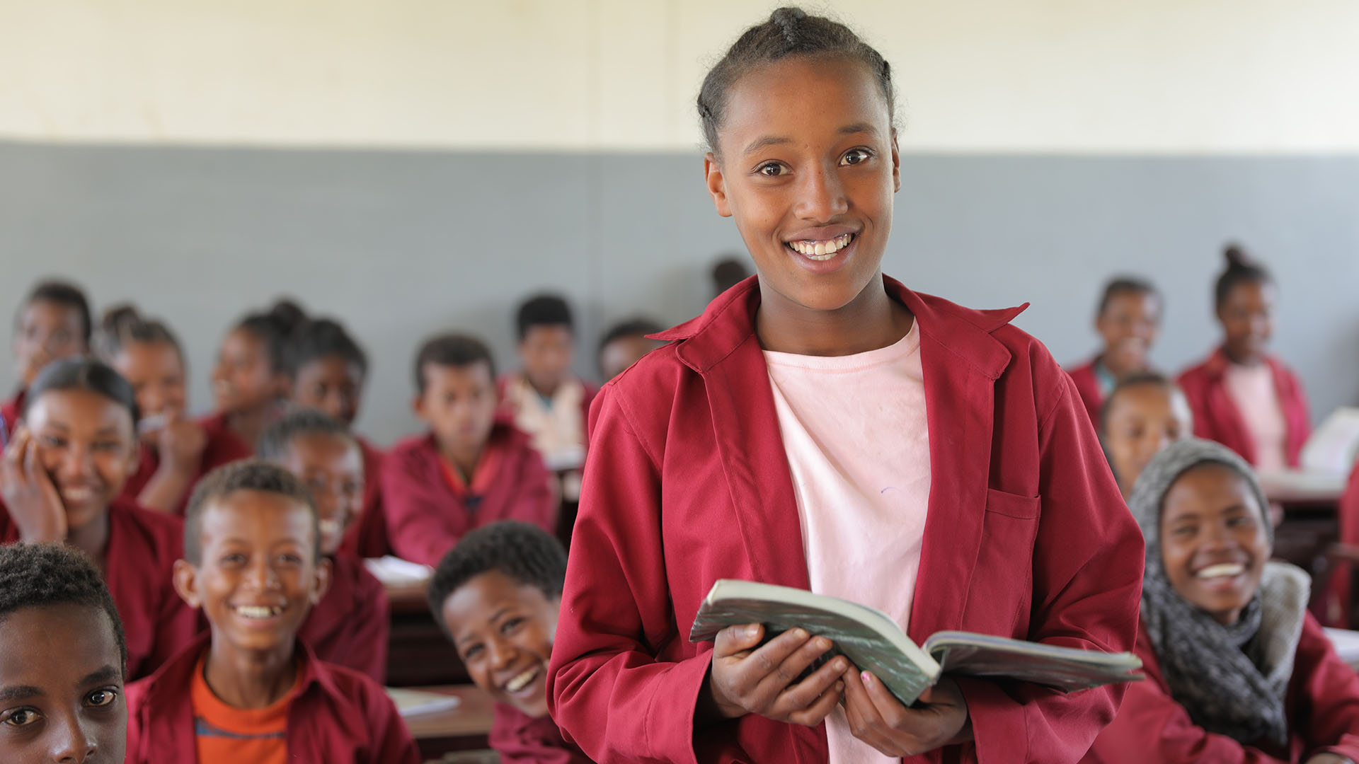 Eine äthiopische Schülerin lächelt mit einem offenen Buch in die Kamera