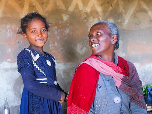 Eine äthiopische Mutter lächert ihre Tochter an, die Tochter lächelt in die Kamera.
