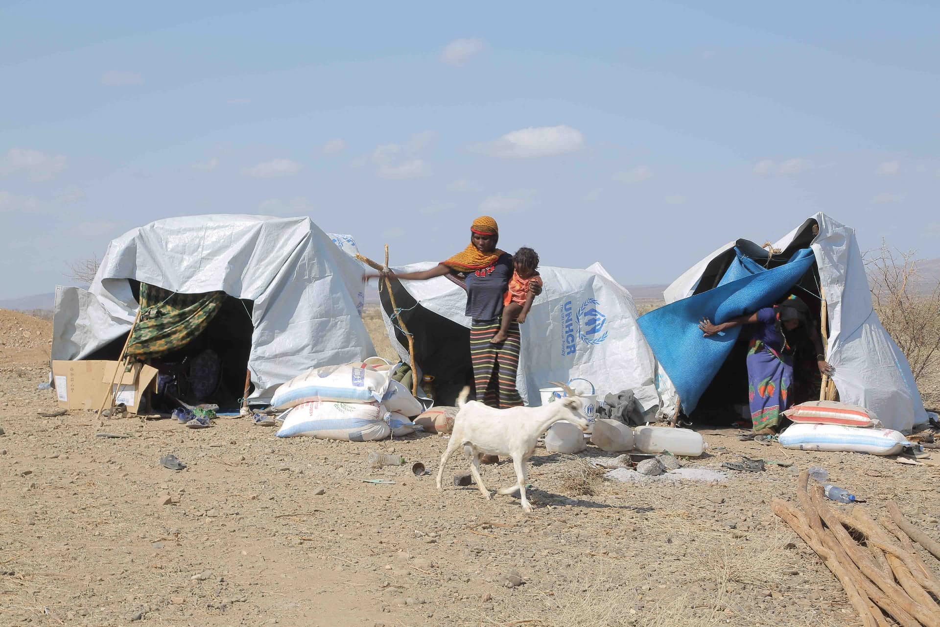 Eine Frau mit einem Kind am Arm steht vor behelfsmäßigen Zelten in einem Flüchtlingslager in Äthiopien