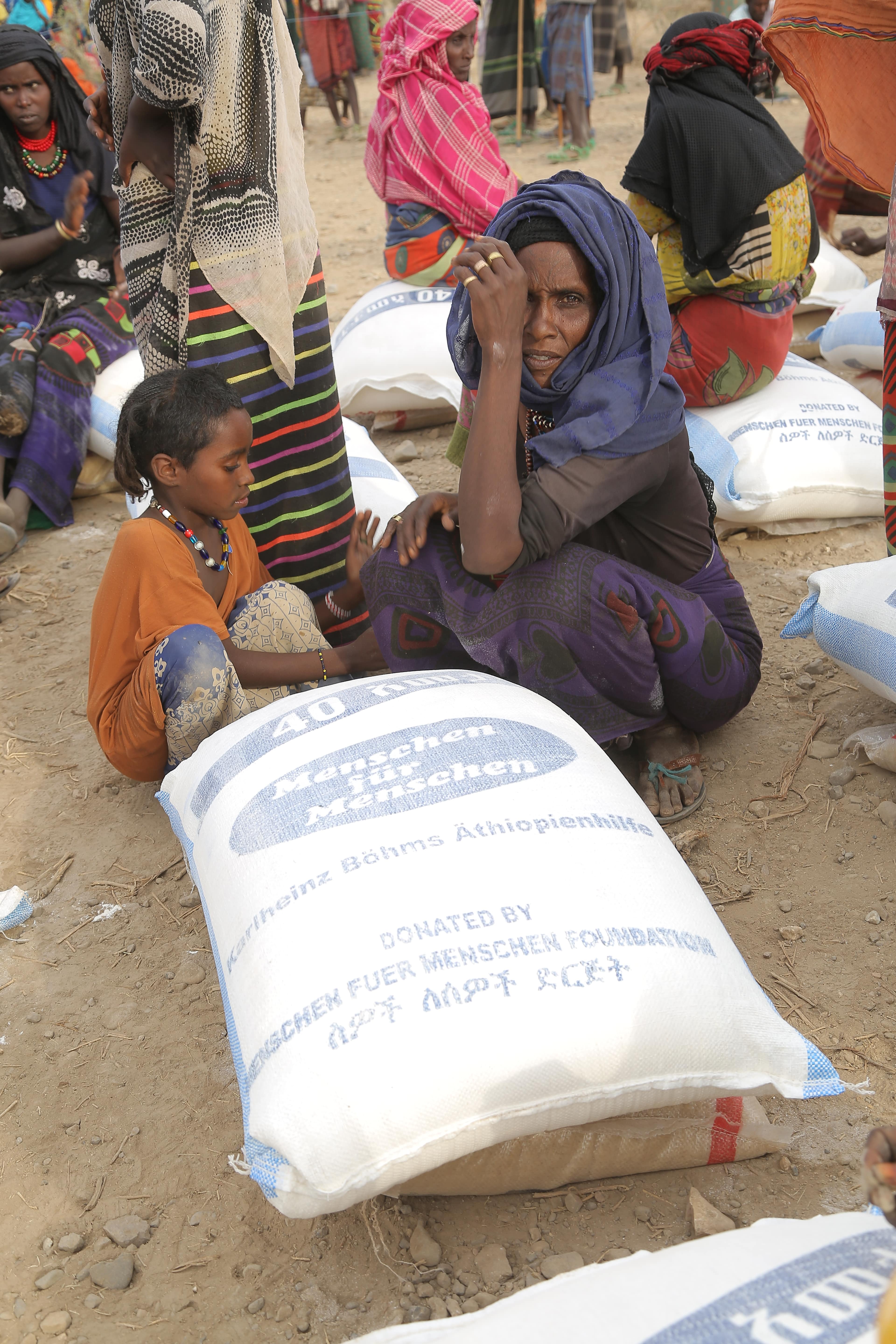 Eine äthiopische Mutter kniet mit ihrem Kind vor einem Sack mit Lebensmittel von Menschen für Menschen