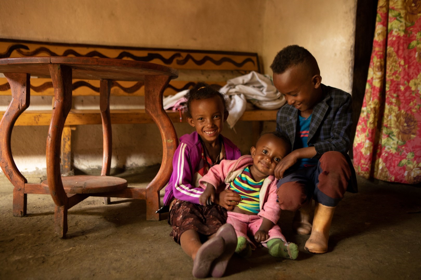 Zwei äthiopische Kleinkinder und ein Baby lächeln am Flur sitzend in die Kamera