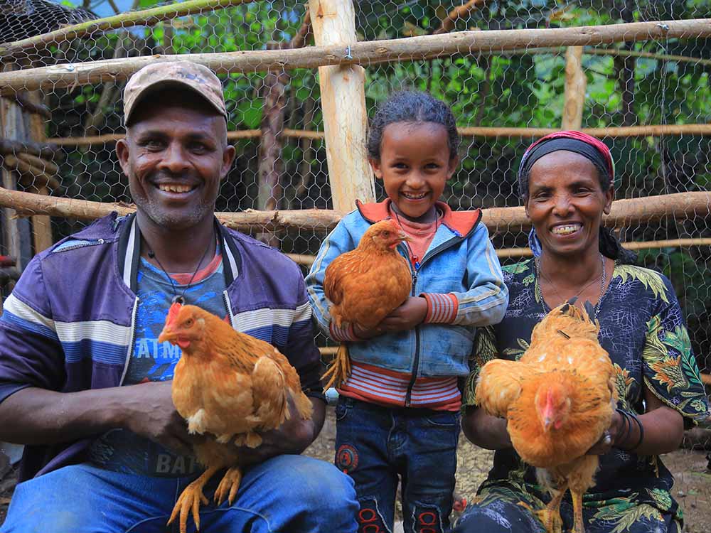 Äthiopische Familie mit Hühnern in der Hand, die in die Kamera lacht.