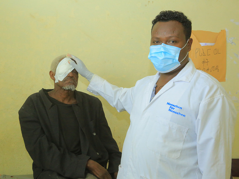 Ein Gesundheitsmitarbeiter von Menschen für Menschen mit einem älteren Mann der nach einer Trichiasis-Operation einen Verband am Auge trägt