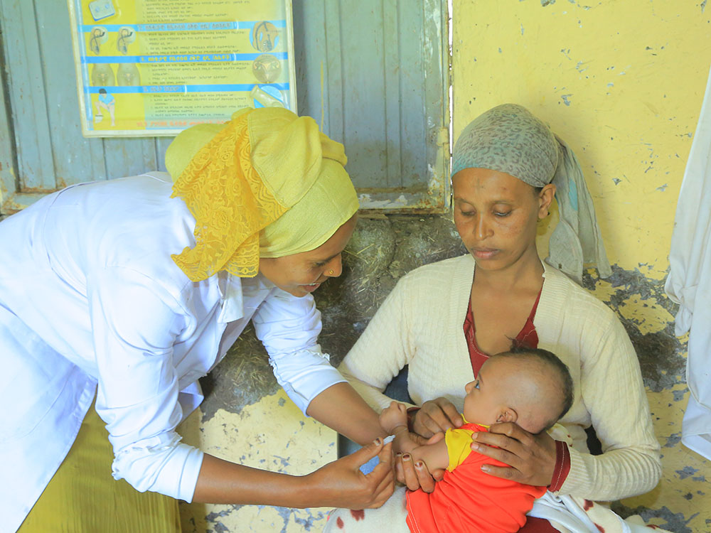 Eine Mutter hält ihr Baby am Schoß während es eine Impfung bekommt