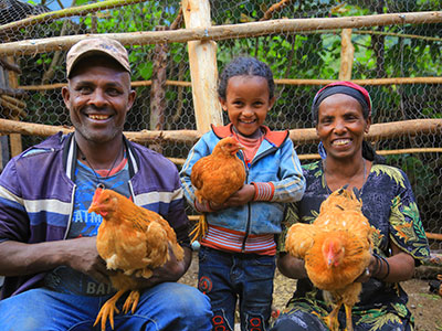Ein Mann, seine Frau und ihre kleine Tochter lächeln in die Kamera. Jeder hält ein Huhn in der Hand