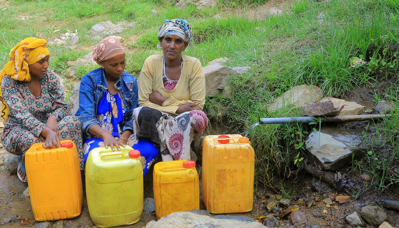 Drei Frauen füllen an einer ungeschützten Wasserstelle Kanister mit Wasser an.