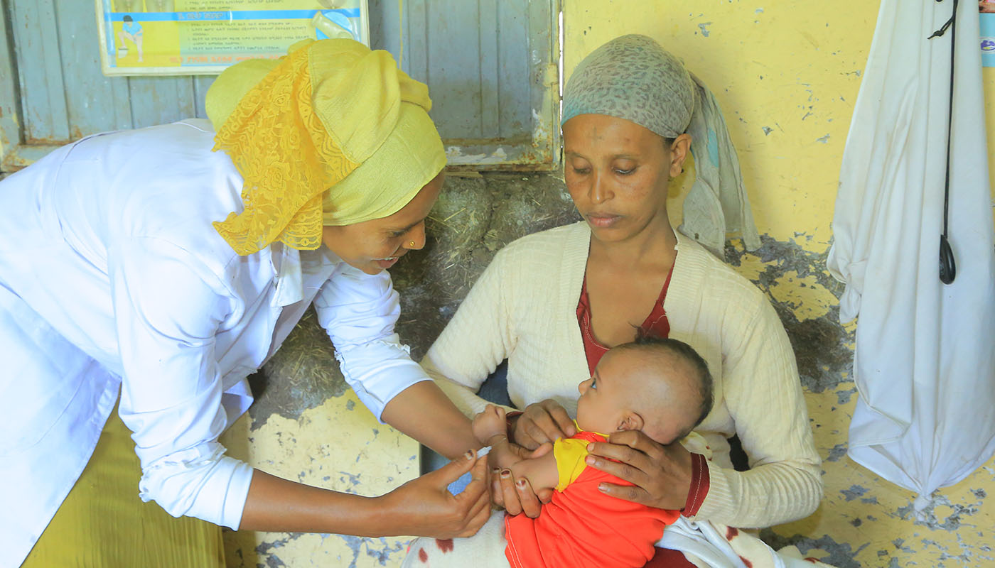 Eine Frau hält ein Kleinkind, das gerade von einer anderen Frau eine Impfung verabreicht bekommt