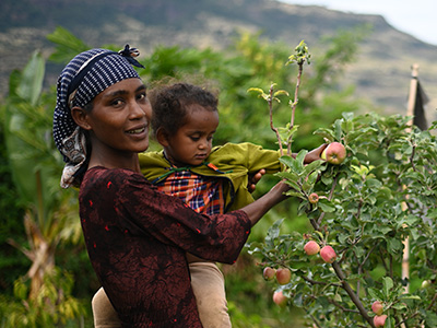 Eine Mutter mit Kind steht neben einem kleinen Apfelbaum
