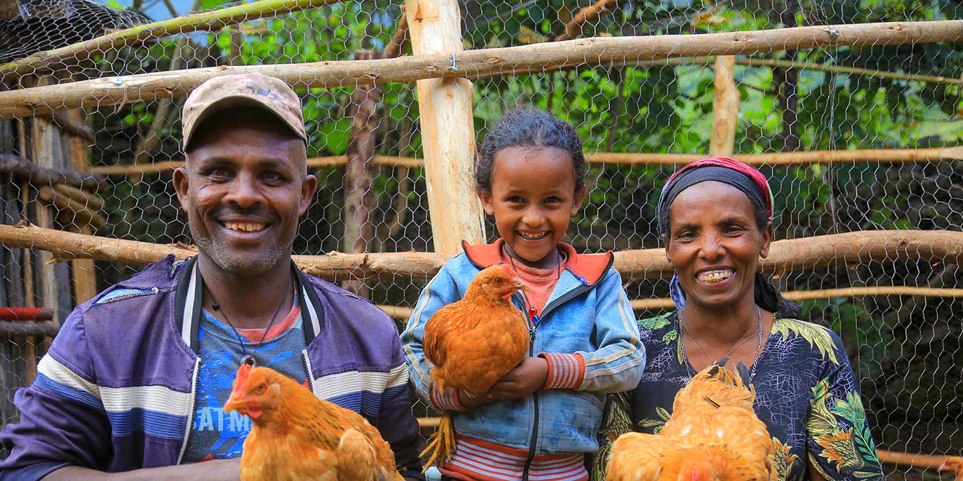 Eine Frau, ihr Mann und ihre kleine Tochter in Äthiopien. Jeder hält ein Huhn in der Hand und lächelt in die Kamera