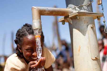 Junges Mädchen trinkt aus neu gebautem Brunnen frisches Trinkwasser