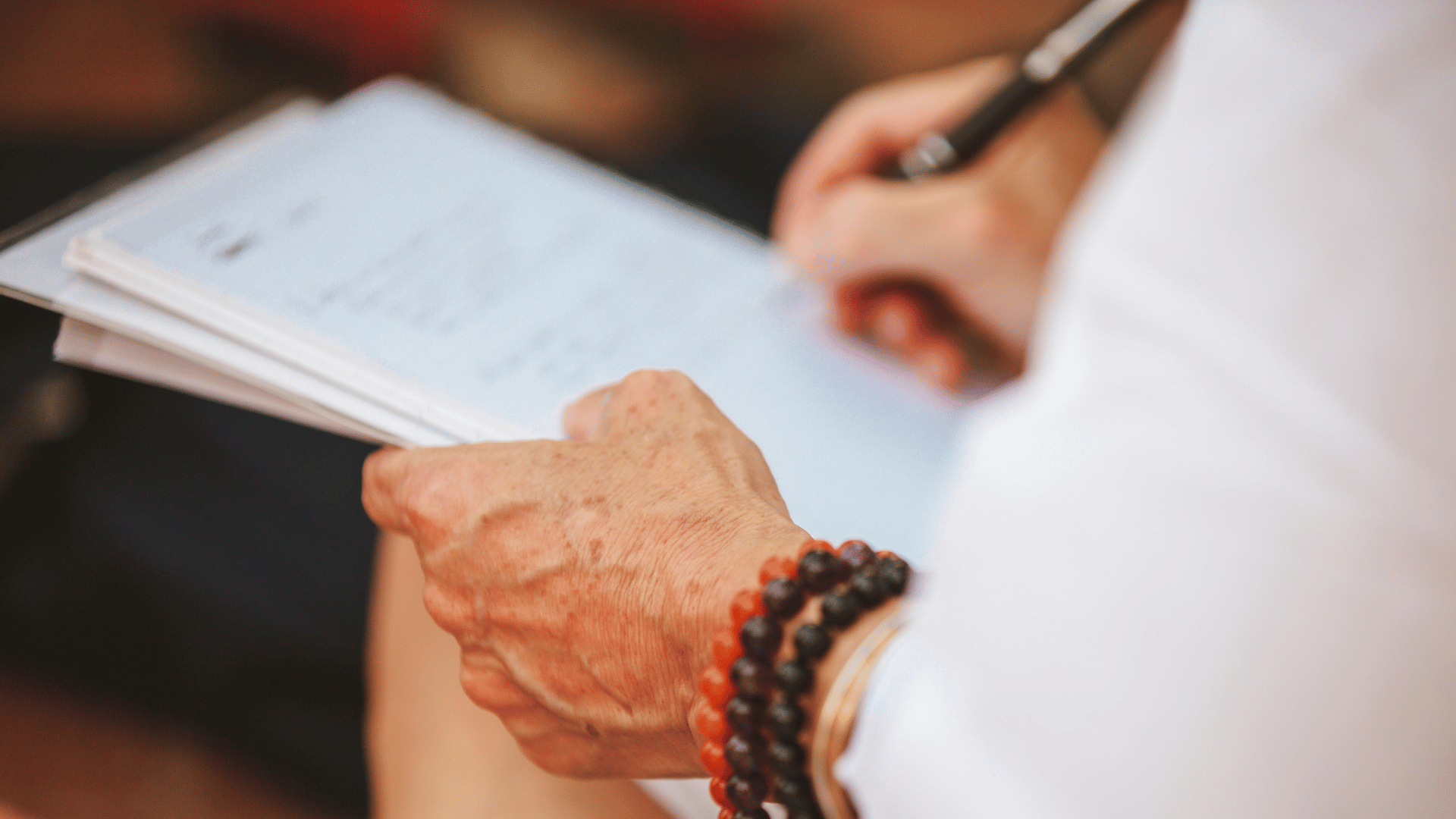 Bildausschnitt von Händen einer älteren Frau, die etwas handschriftlich festhält