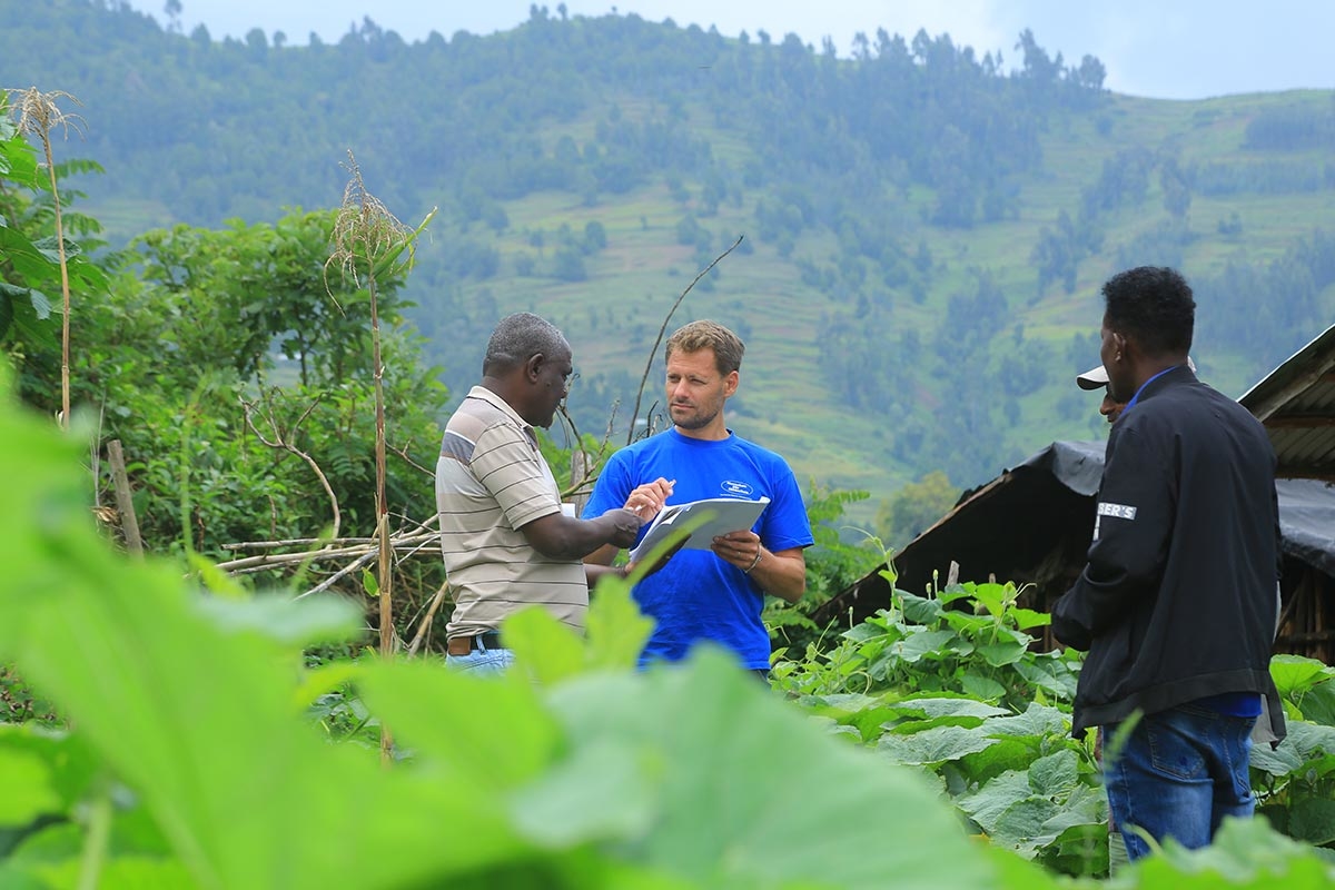 Markus Schwarz-Herda im blauen T-Shirt im Gespräch mit Projektleiter Berhanu Bedassa und einem weiteren Kollegen in einer grünen, hügeligen Landschaft in Äthiopien. Sie begutachten gemeinsam Unterlagen.