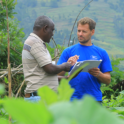 Markus Schwarz-Herda im blauen T-Shirt im Gespräch mit Projektleiter Berhanu Bedassa in einer grünen, hügeligen Landschaft in Äthiopien. Sie begutachten gemeinsam Unterlagen.