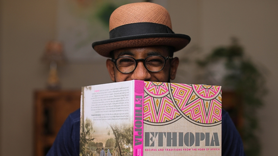 Yohanis Gebreyesus hält sein aufgeschlagenes Kochbuch „Ethiopia“ vor das Gesicht und blickt darüber hinweg.