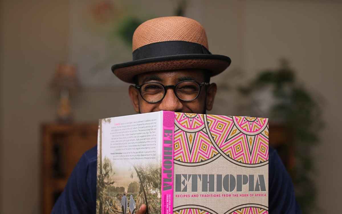 Yohanis Gebreyesus hält sein aufgeschlagenes Kochbuch „Ethiopia“ vor das Gesicht und blickt darüber hinweg.