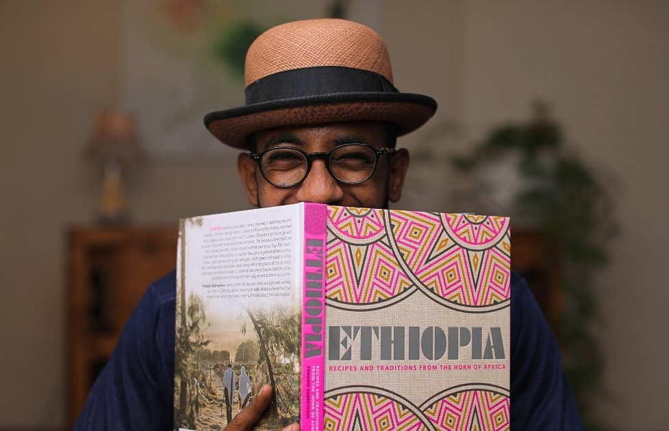 Yohanis Gebreyesus hält sein aufgeschlagenes Kochbuch „Ethiopia“ vor das Gesicht und blickt darüber hinweg.