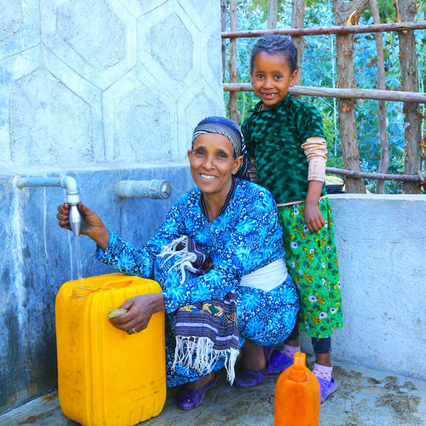 Fatiya und ihre Mutter Alem füllen an einer Quellfassung frisches Wasser in gelbe Kanister.