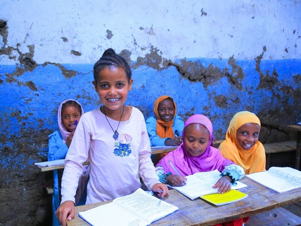 Schülerinnen sitzen im Klassenzimmer an ihren Schreibtischen und schreiben in ihre Hefte.