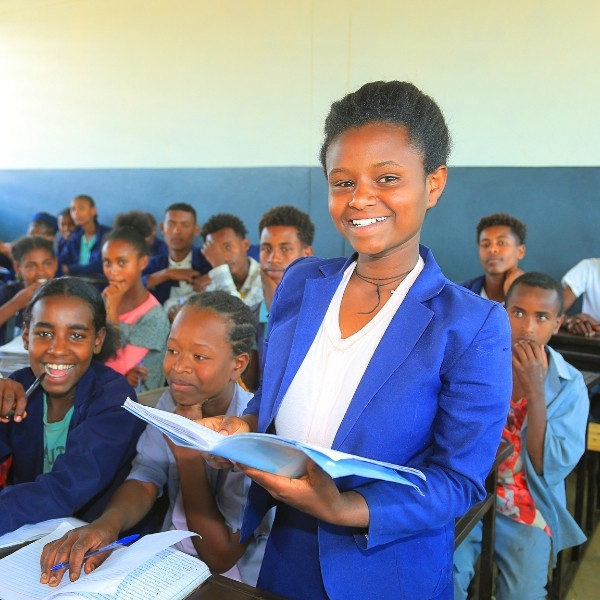 Eine Schülerin steht an ihrem Tisch im Klassenzimmer und liest in einem Buch.