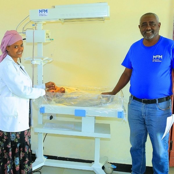 Projektkoordinator Berhanu Badessa steht gemeinsam mit einer Hebamme an einem Wärmebett, in dem ein Baby schläft.