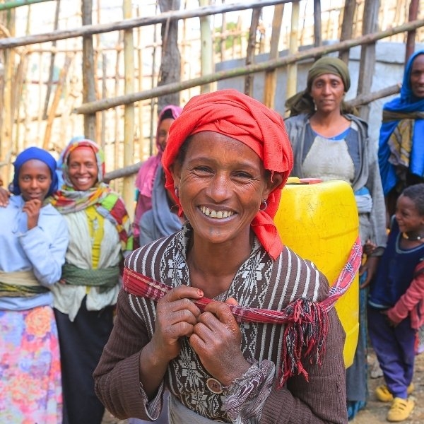 Eine Frau trägt auf ihrem Rücken einen gelben Wasserkanister.