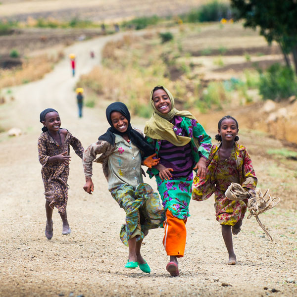Lachend laufen vier Kinder über einen Feldweg.