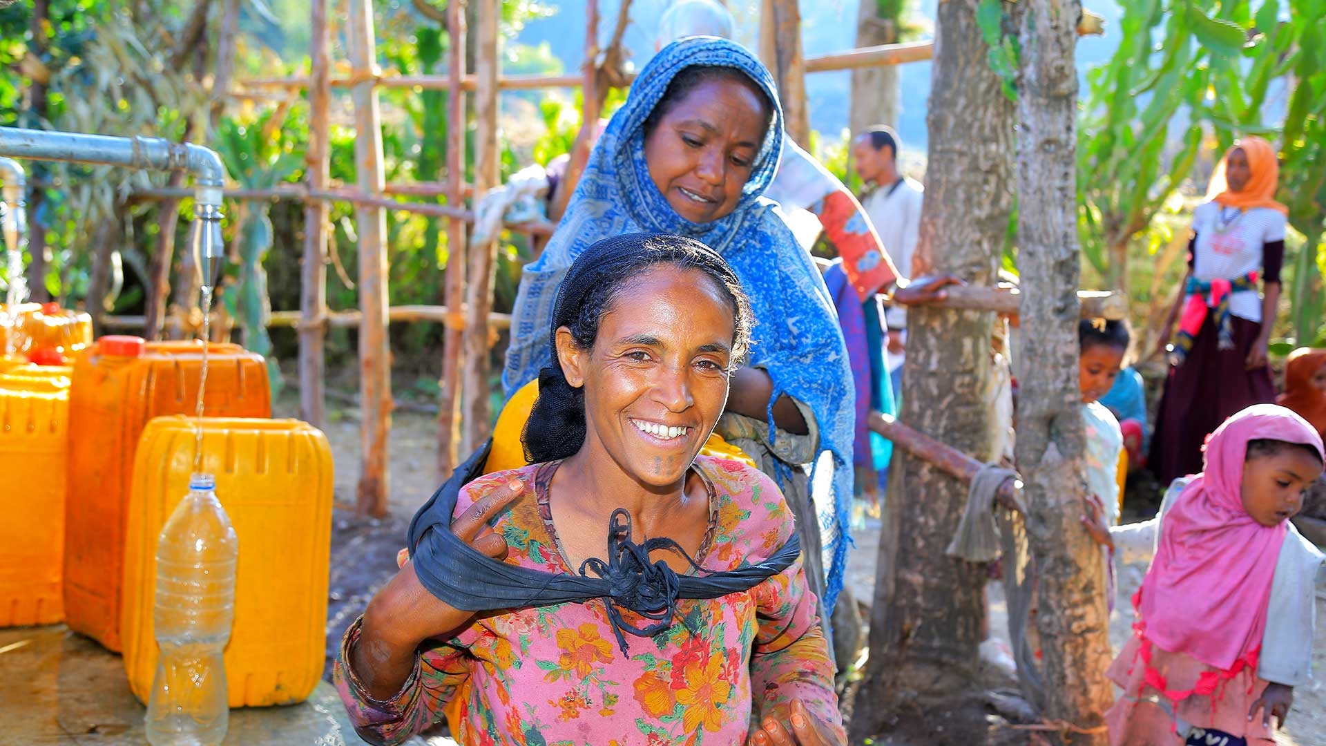 Eine Frau trägt auf dem Rücken einen gelben Wasserkanister.