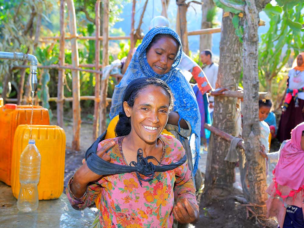 Eine Frau trägt auf dem Rücken einen gelben Wasserkanister.