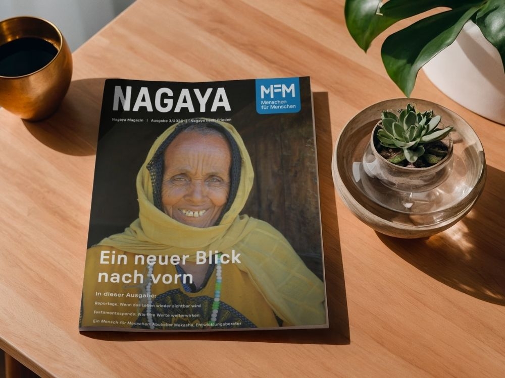Eine ältere Frau, die sich lächelnd an einen Türstock lehnt und direkt in die Kamera blickt.