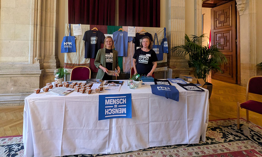 Mitarbeiterinnen von Menschen für Menschen verkaufen T-Shirts und Taschen im neuen Design.
