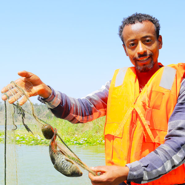 Ein junger Mann in orangefarbener Schwimmweste hält einen Fisch in seinem Netz.