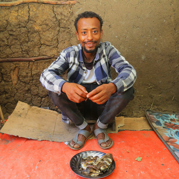 Ein Mann hockt am Boden und präsentiert eine Platte mit frisch gebratenen Fischen.