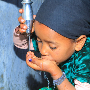 Ein äthiopisches Kind trinkt sauberes Trinkwasser aus einer Quellfassung.