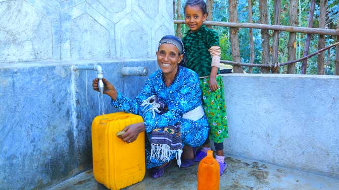 Eine Frau und ein Kind befinden sich an einer Quellfassung in Äthiopien, um sauberes Trinkwasser in ihre gelben Kanister zu füllen.