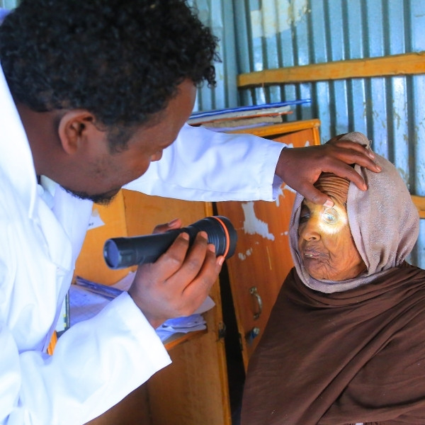 Ein Arzt untersucht das Auge einer Patientin, indem er mit einer Taschenlampe hineinleuchtet.
