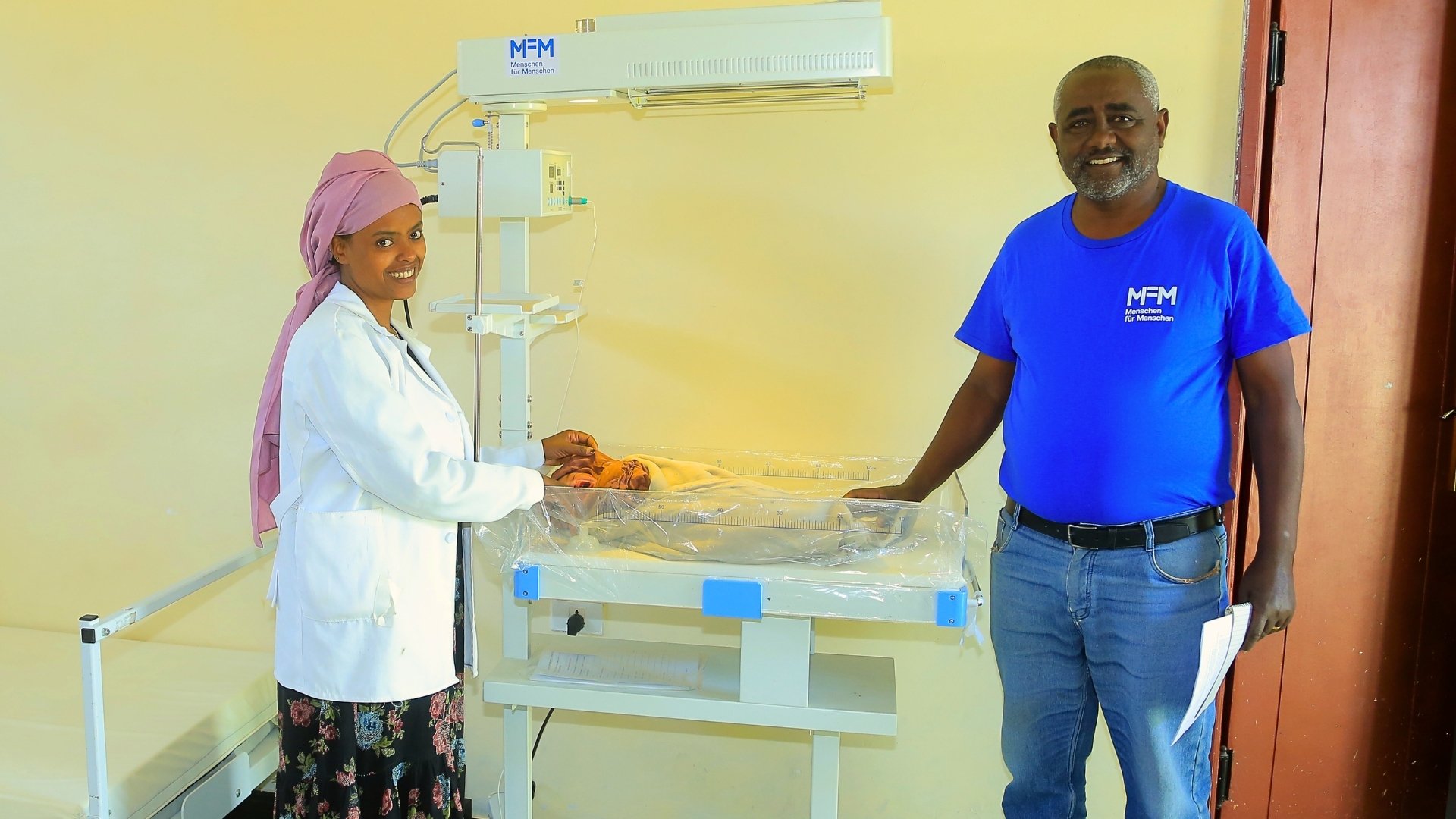 Hebamme Hayat Adem und Projektleiter Berhanu Bedassa beim kleinen Abduraman, der friedlich und geborgen unter dem Wärmestrahler schläft.