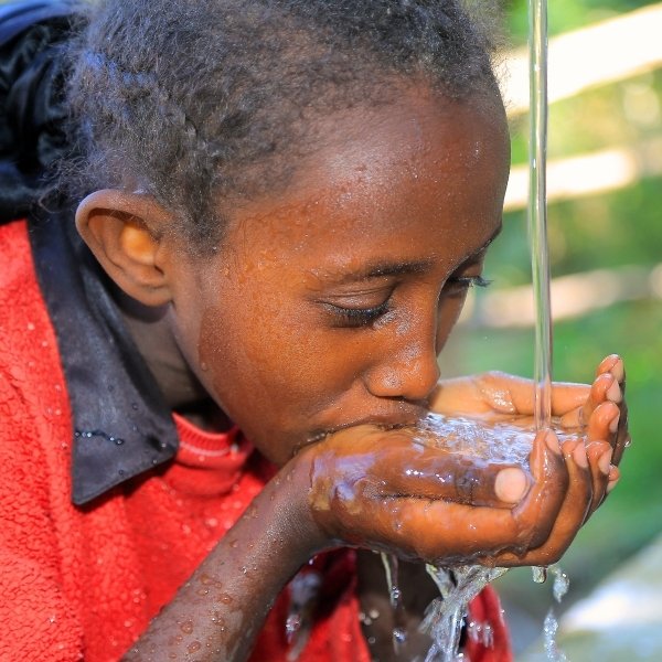 Ein Kind trinkt frisches Wasser aus einer Quellfassung.