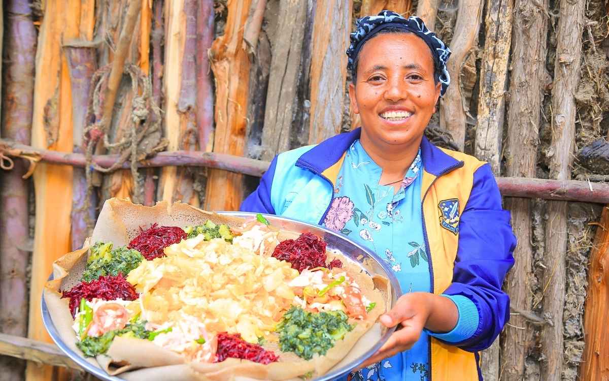 Eine Frau hält einen große Schale mit Injera und unterschiedlichen Eintöpfen in ihren Händen.